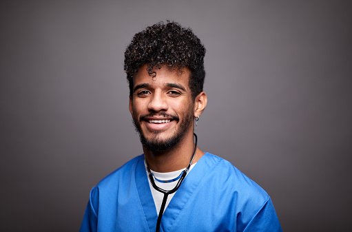 A younger doctor in blue scrubs smiling
