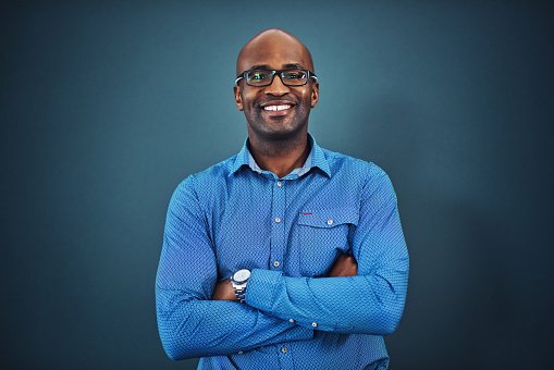 A GP in a blue shirt smiling with arms crossed